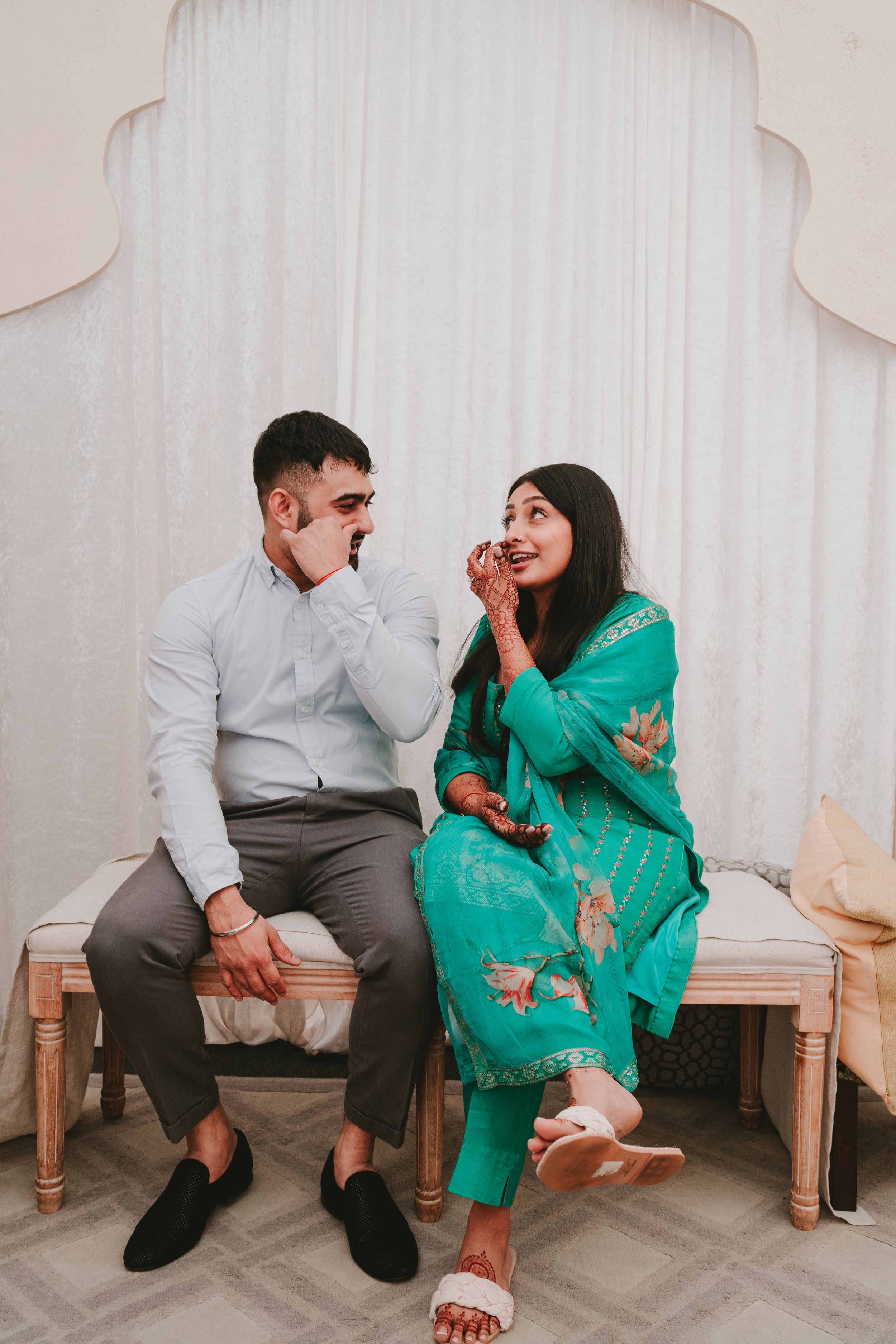 Couple sharing a joyful moment while seated on bench in traditional Indian attire.
