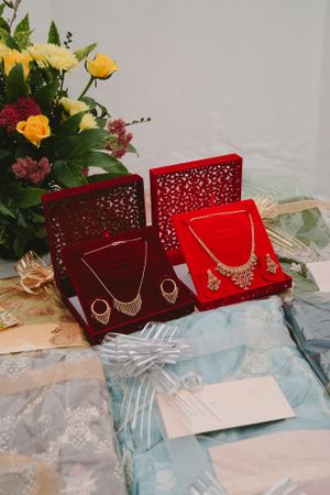 Elegant jewelry displayed in red velvet boxes alongside fresh floral arrangements.