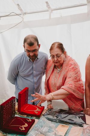 Two people examining jewelry pieces from red display box during traditional celebration.