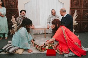 Group sits on floor playing a traditional game during cultural celebration with wooden board and pieces.