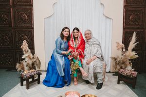 Three generations pose together in traditional attire during a South Asian wedding celebration.