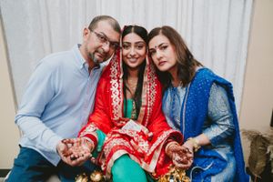 Family members gather around the bride wearing traditional South Asian attire in red and blue.