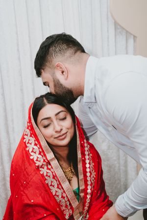 A tender moment during a traditional South Asian wedding ceremony with a bride wearing an elegant red embroidered dupatta.