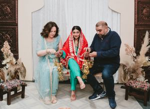 Wedding ceremony moment with guests in traditional attire seated against ornate backdrop with pampas grass decor.