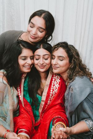 Tender group moment during a wedding celebration with traditional South Asian attire and henna decorated hands.