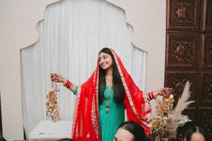 Traditional South Asian bride in vibrant red and green attire standing against an ornate backdrop.