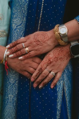 Wedding rings and henna designs displayed on hands over blue embellished fabric.