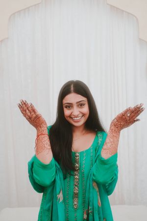 Festive pose showing decorated henna hands against white architectural backdrop.