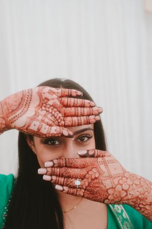 Intricate henna designs on hands displayed in front of face against white background.