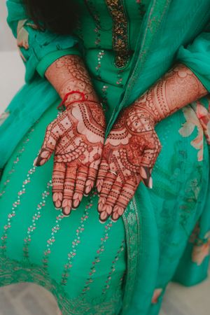 Detailed mehndi patterns on palms displayed over emerald green traditional dress.