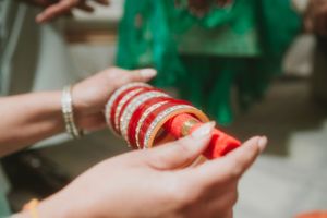 Hands with bracelets holding red and gold bangles in preparation for an Indian wedding ceremony.
