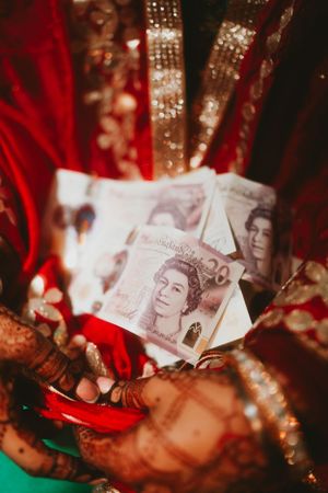 Henna-decorated hands holding British pound notes against red and green fabric.