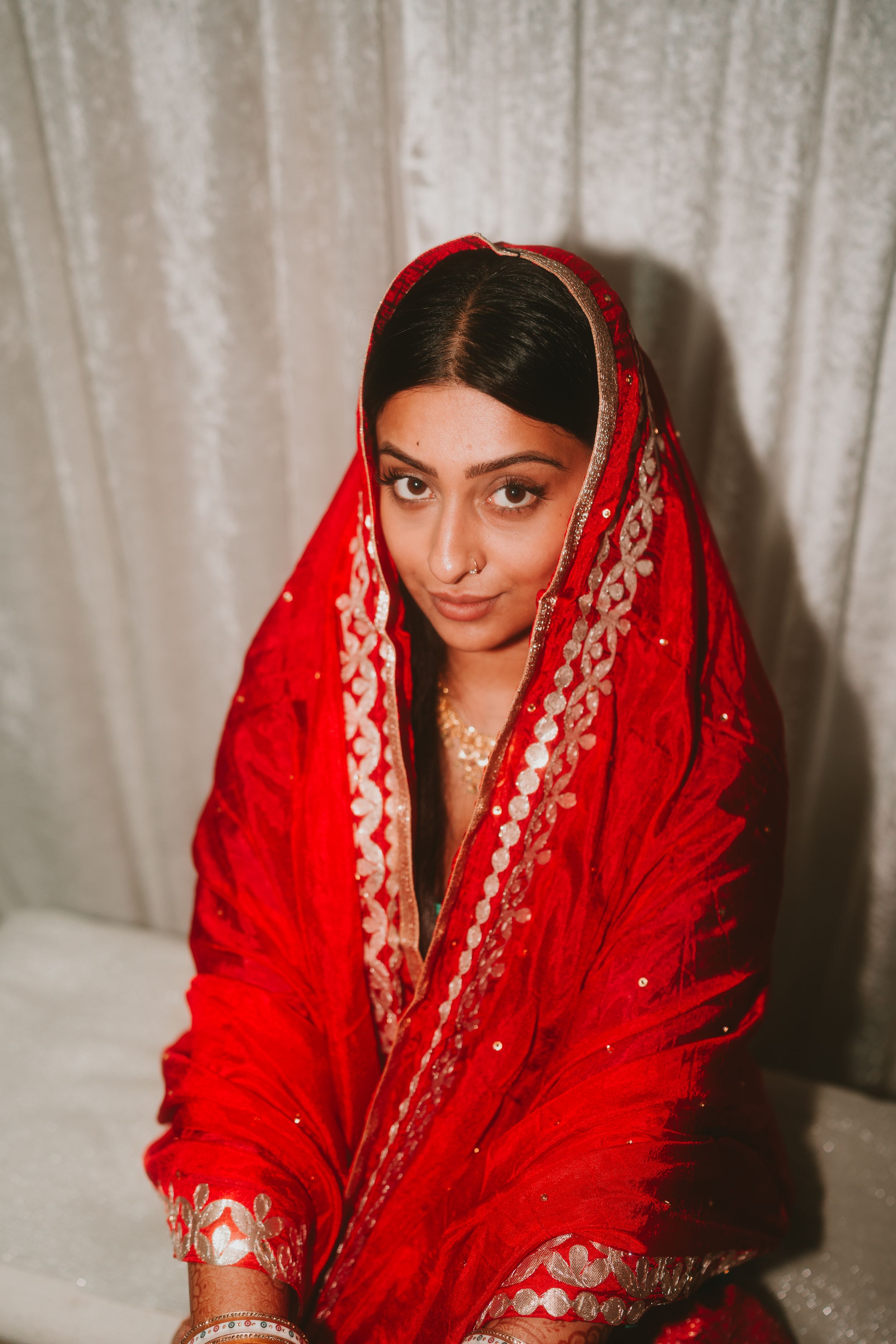 A person wearing a red embroidered dupatta poses in traditional South Asian bridal attire.