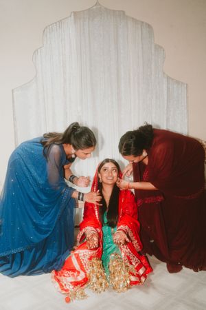 Three people in traditional South Asian clothing share a candid moment during wedding preparations.