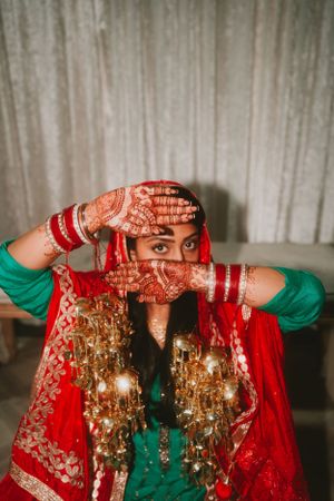Person in traditional red and green attire shows intricate henna designs on their hands.