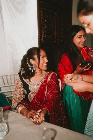 Women in traditional red and green Indian attire enjoying a celebration together.