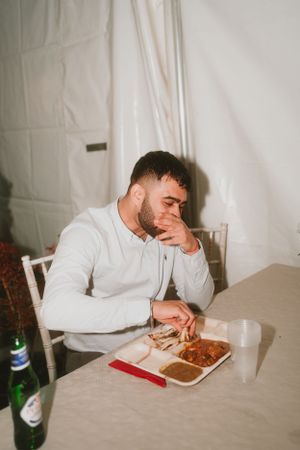Person in white sweater sitting alone at table with takeout food.