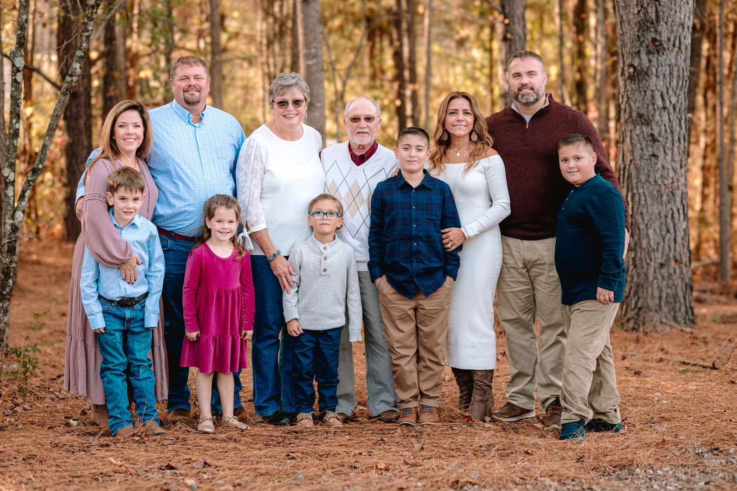 Extended family gathering outdoors in coordinated outfits among pine trees.
