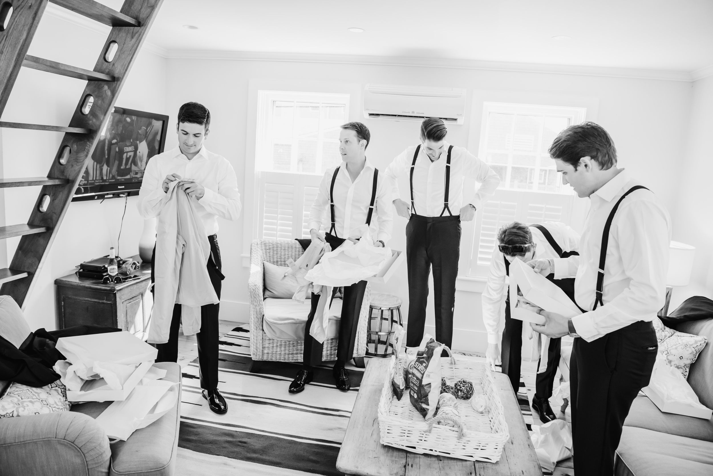 Groomsmen in white shirts and suspenders getting ready in a bright room.