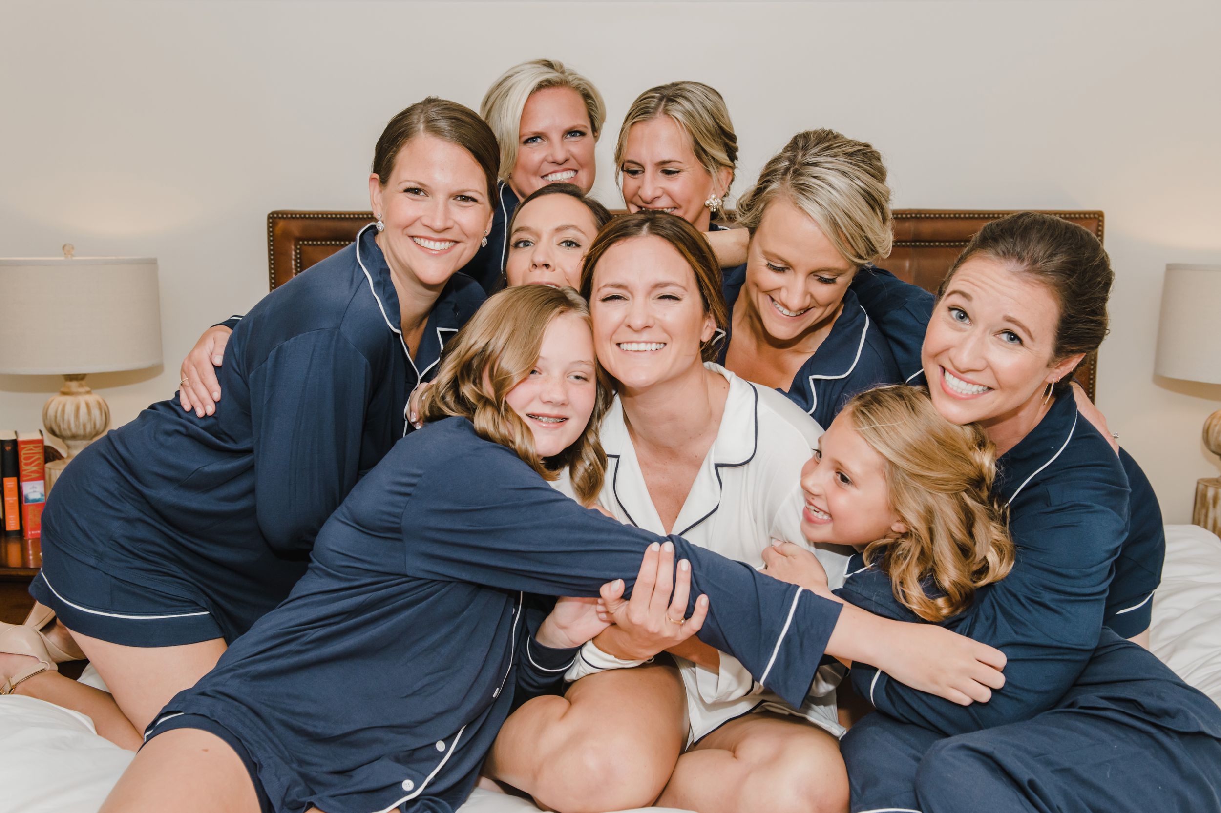 Bridesmaids in matching navy robes share a fun group moment on a bed.