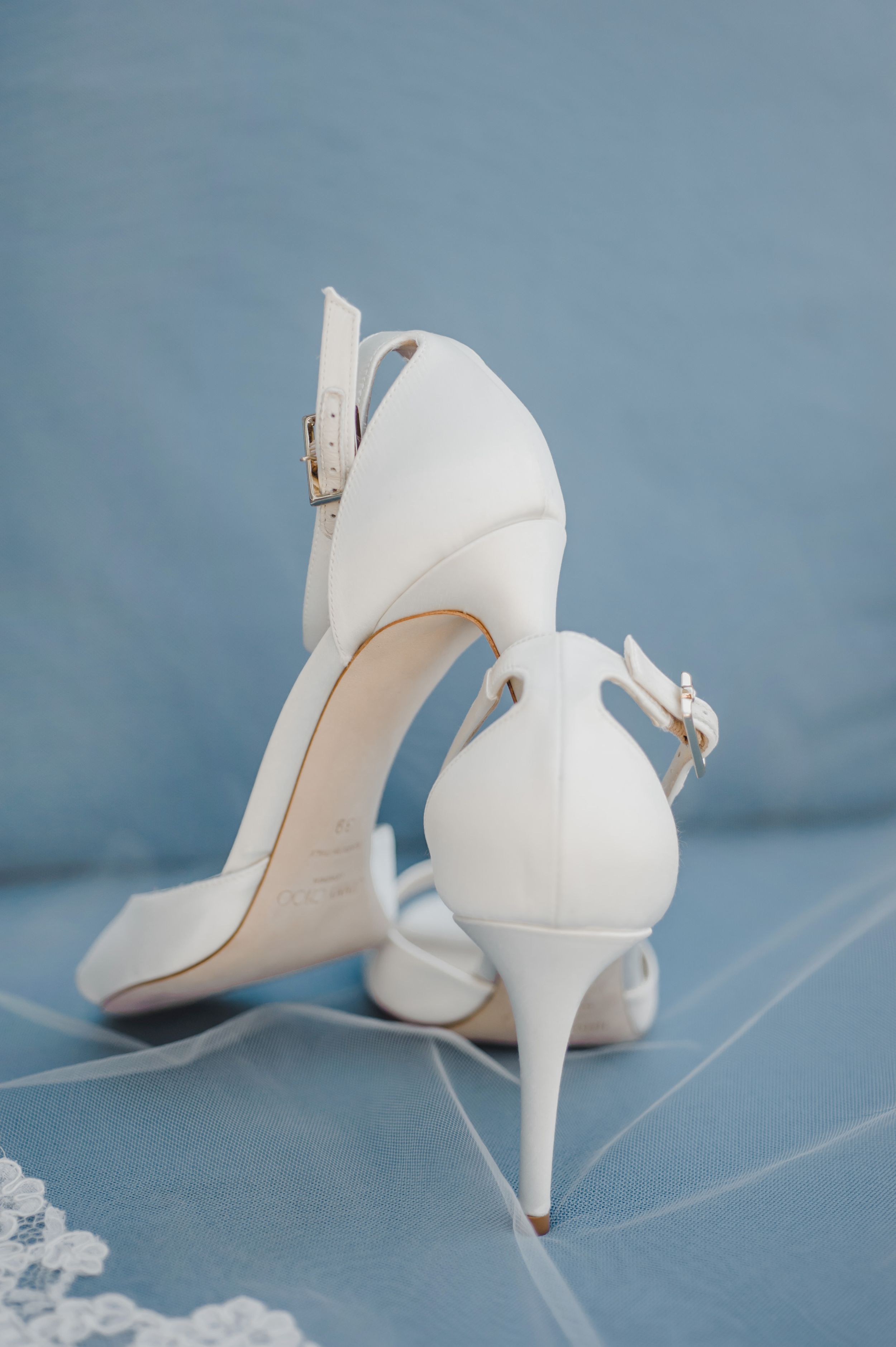 Elegant white bridal heels with buckle details against a blue background.