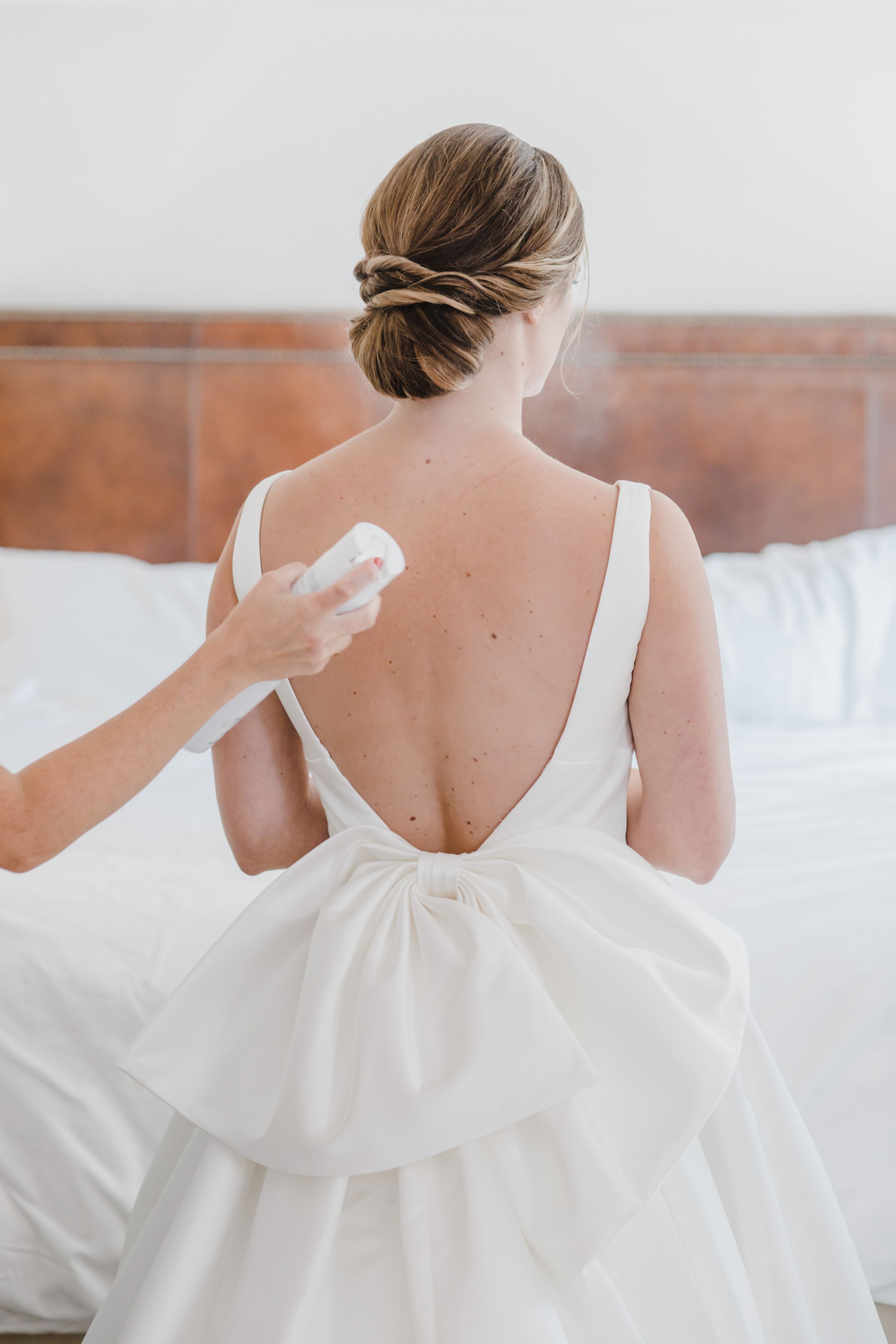 Back view of a white wedding dress being prepared with elegant hair styling.