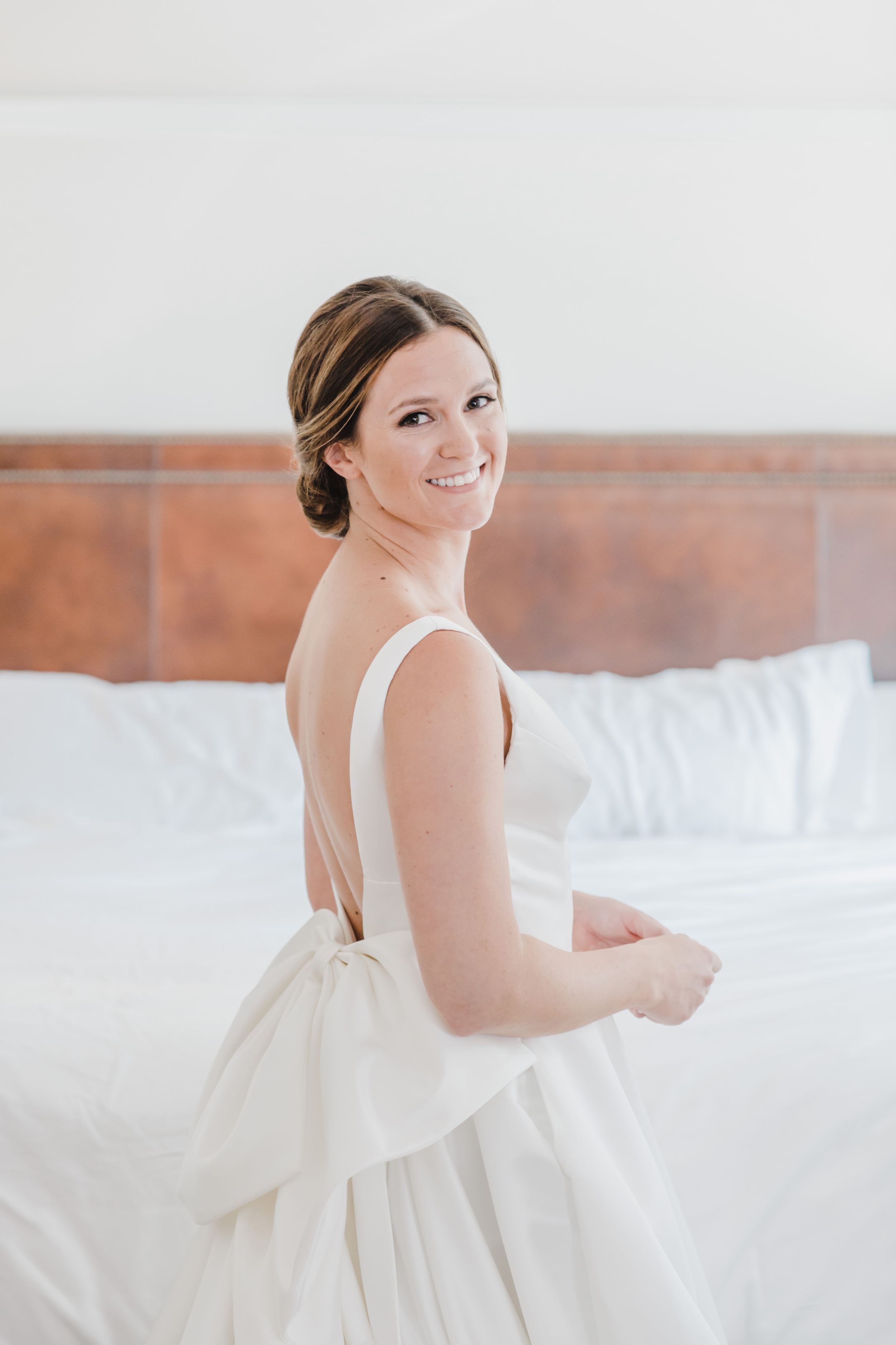 Bride in a classic white wedding gown with v-neck design smiles in a bright room.