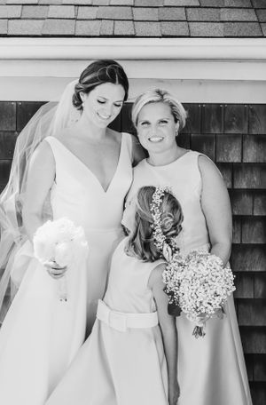 Wedding party members in elegant dresses share a joyful moment while holding white bouquets.