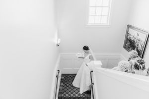 A wedding dress flows down white stairs in a bright interior setting.