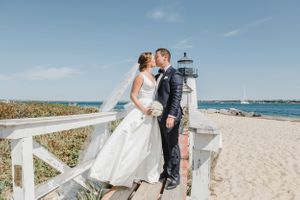 Romantic lighthouse wedding portrait on a sandy beach with white wooden railings.