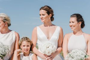A small wedding party group poses with white bouquets against a bright blue sky.