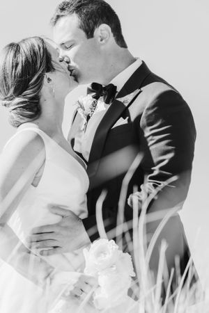Black and white romantic portrait of couple embracing through tall grass.