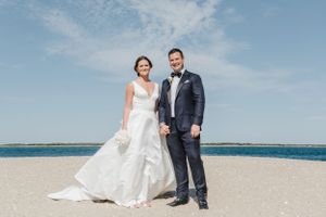 Wedding couple poses on beach with ocean and blue sky in background.