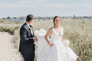 Wedding couple walking along a sandy beach path with flowing white dress.