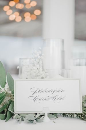 Elegant place card for Philadelphia Cricket Club with greenery accents and bokeh lighting.