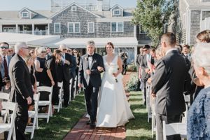 Wedding ceremony taking place on a manicured lawn with white chairs and coastal homes in the background.