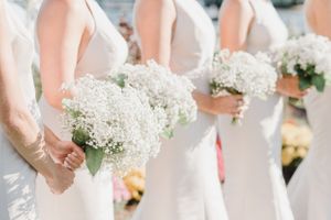 Row of bridesmaids in white dresses holding baby's breath bouquets.
