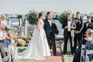 Outdoor waterfront wedding ceremony with guests seated on white chairs.