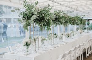 Long reception tables adorned with elevated greenery arrangements and white place settings.