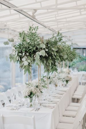 Elegant wedding table decor with tall greenery centerpieces and white linens.