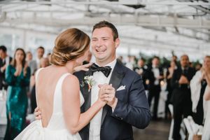 A couple shares their first dance at an elegant wedding reception under a white tent.