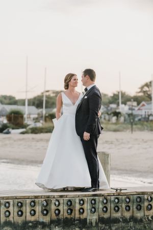 Wedding couple posing on vintage dock with nautical elements and coastal scenery.