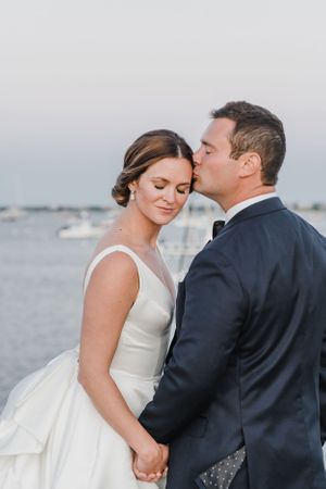Intimate wedding portrait by the water during sunset with boats in background.