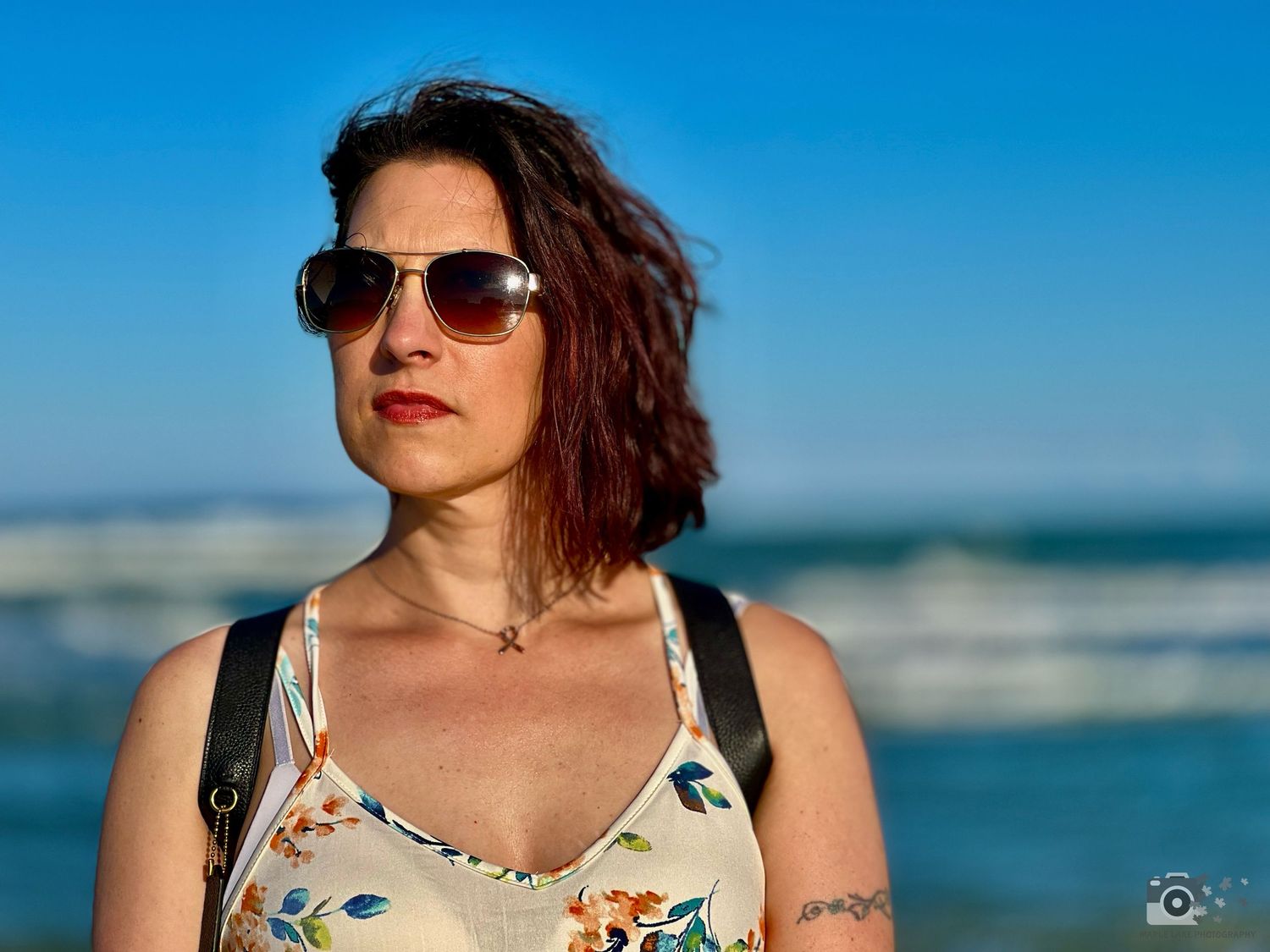 A summer beach portrait featuring sunglasses and a floral tank top against blue skies.