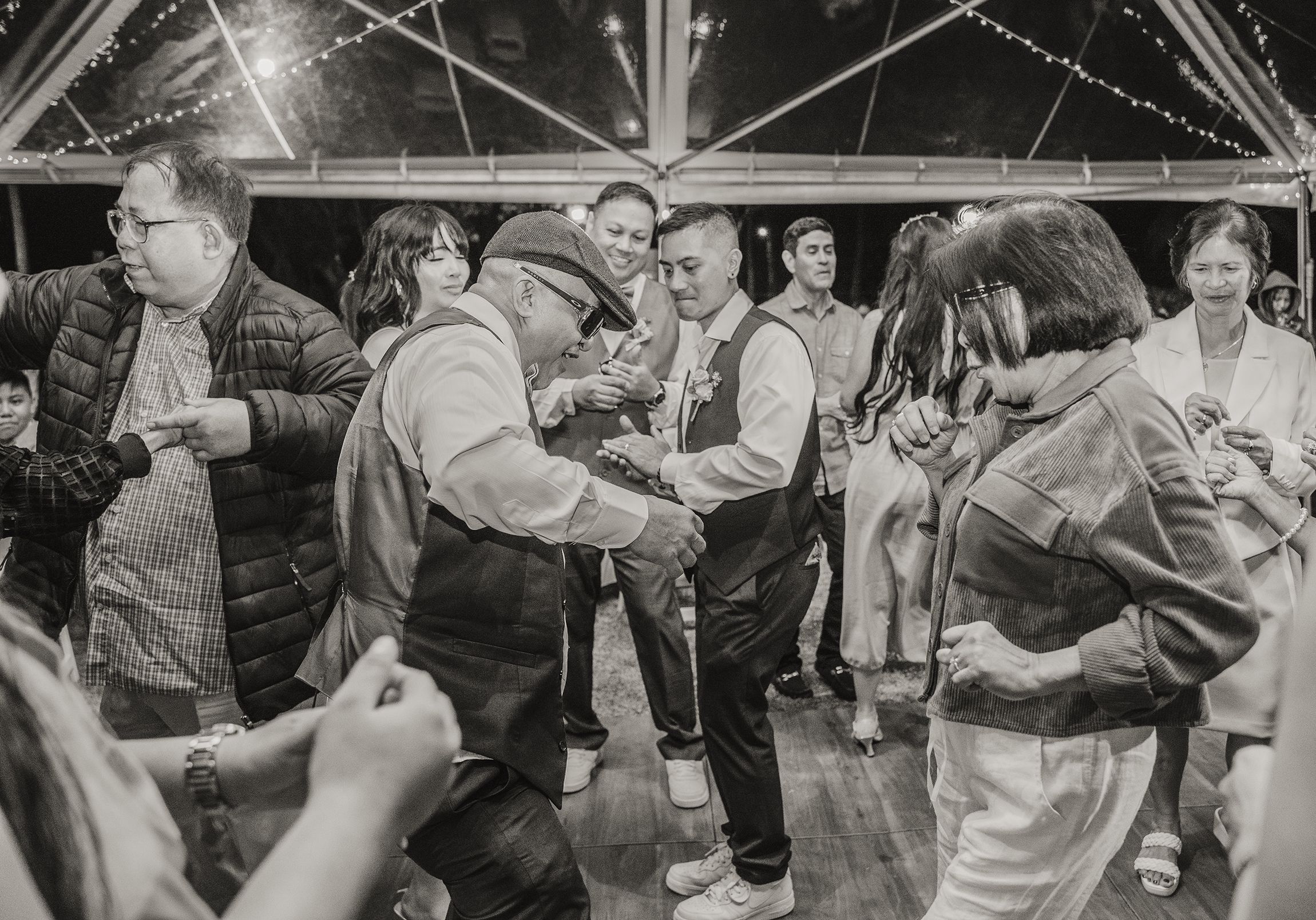 Black and white photo of guests dancing and having fun at a party on a dance floor with a beamed ceiling.