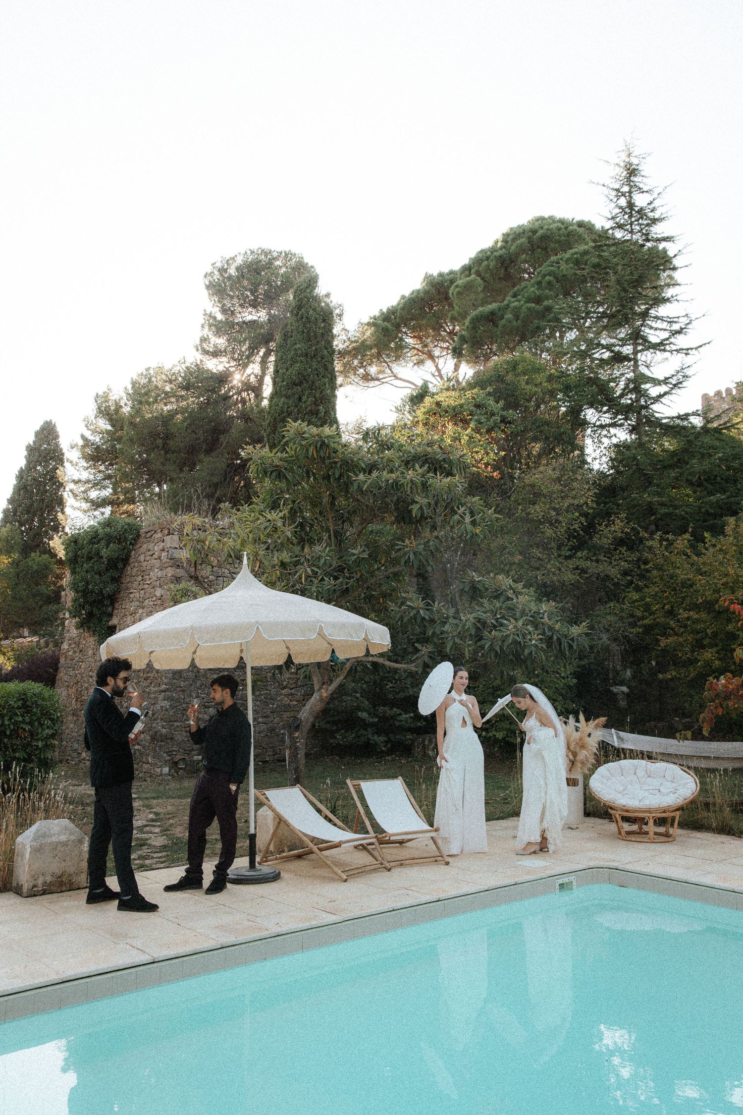 A newlywed couple walks hand in hand through a Mediterranean-style garden setting.