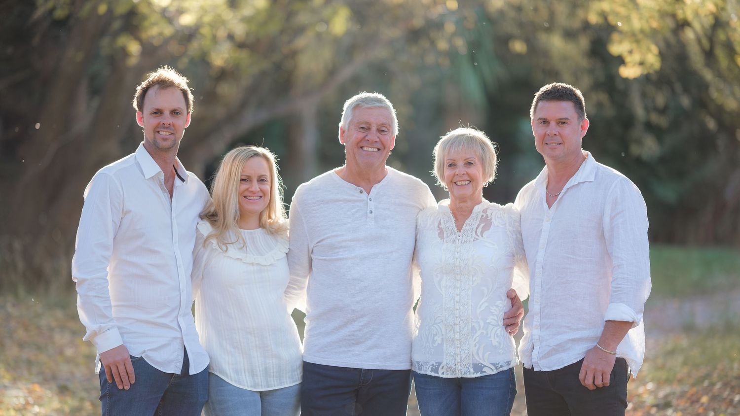 Group photo of family members all wearing coordinated white outfits outdoors.