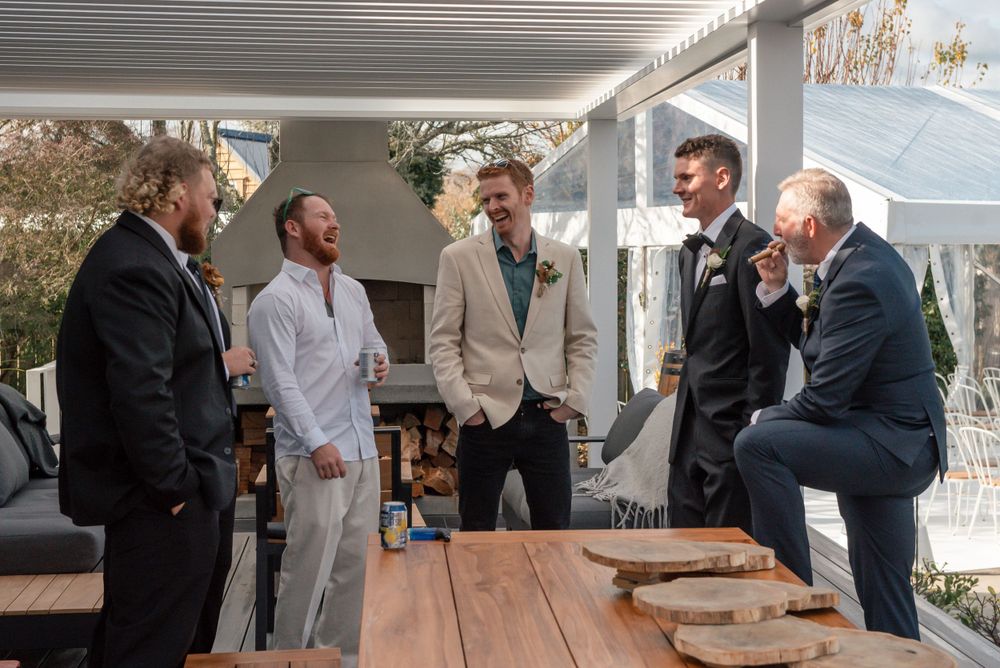 Groomsmen share laughs during pre-wedding preparations on an outdoor porch Cambridge Hamilton New Zealand