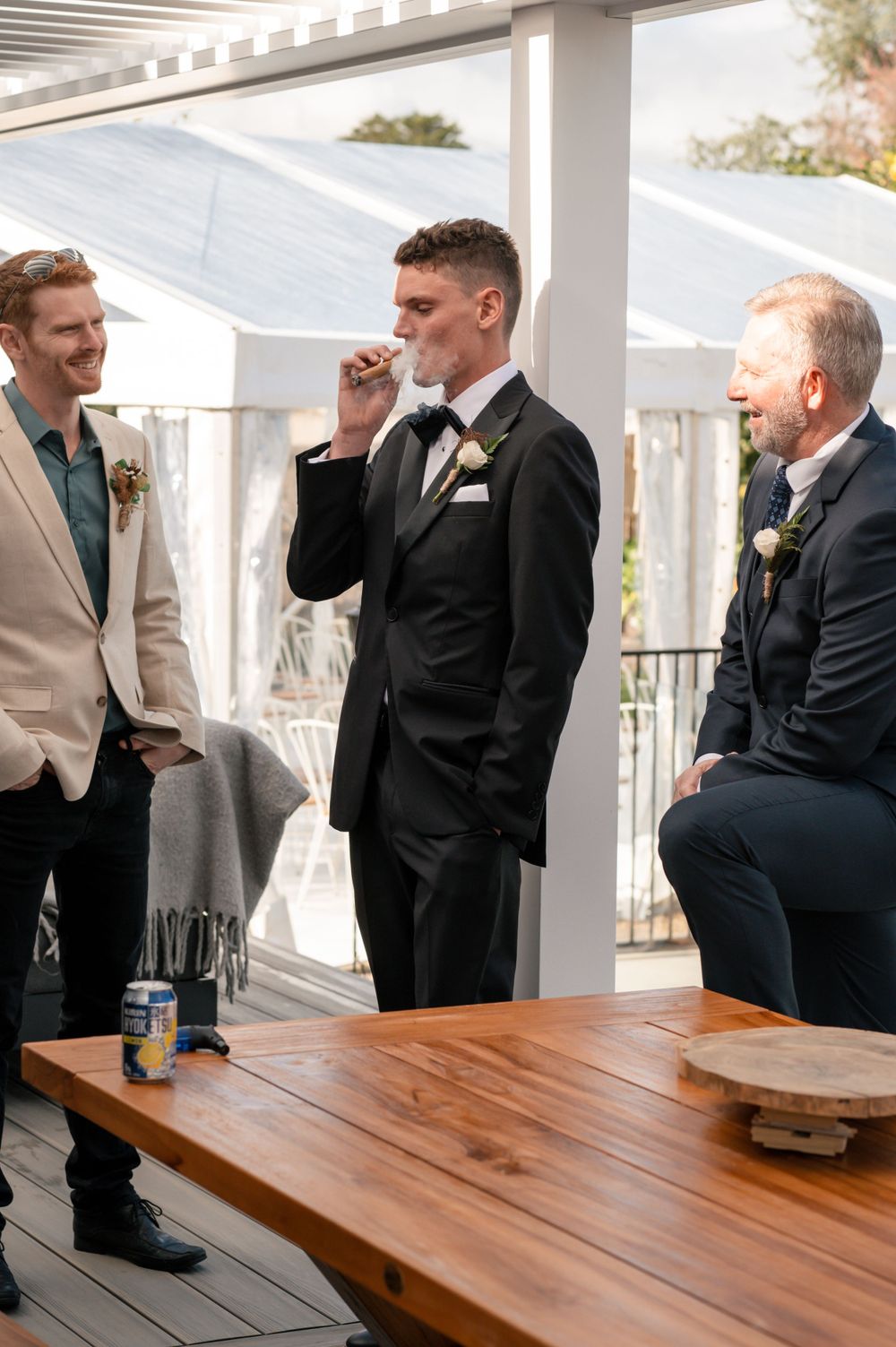 Groomsmen share drinks and conversation on a covered porch before the ceremony Cambridge New Zealand