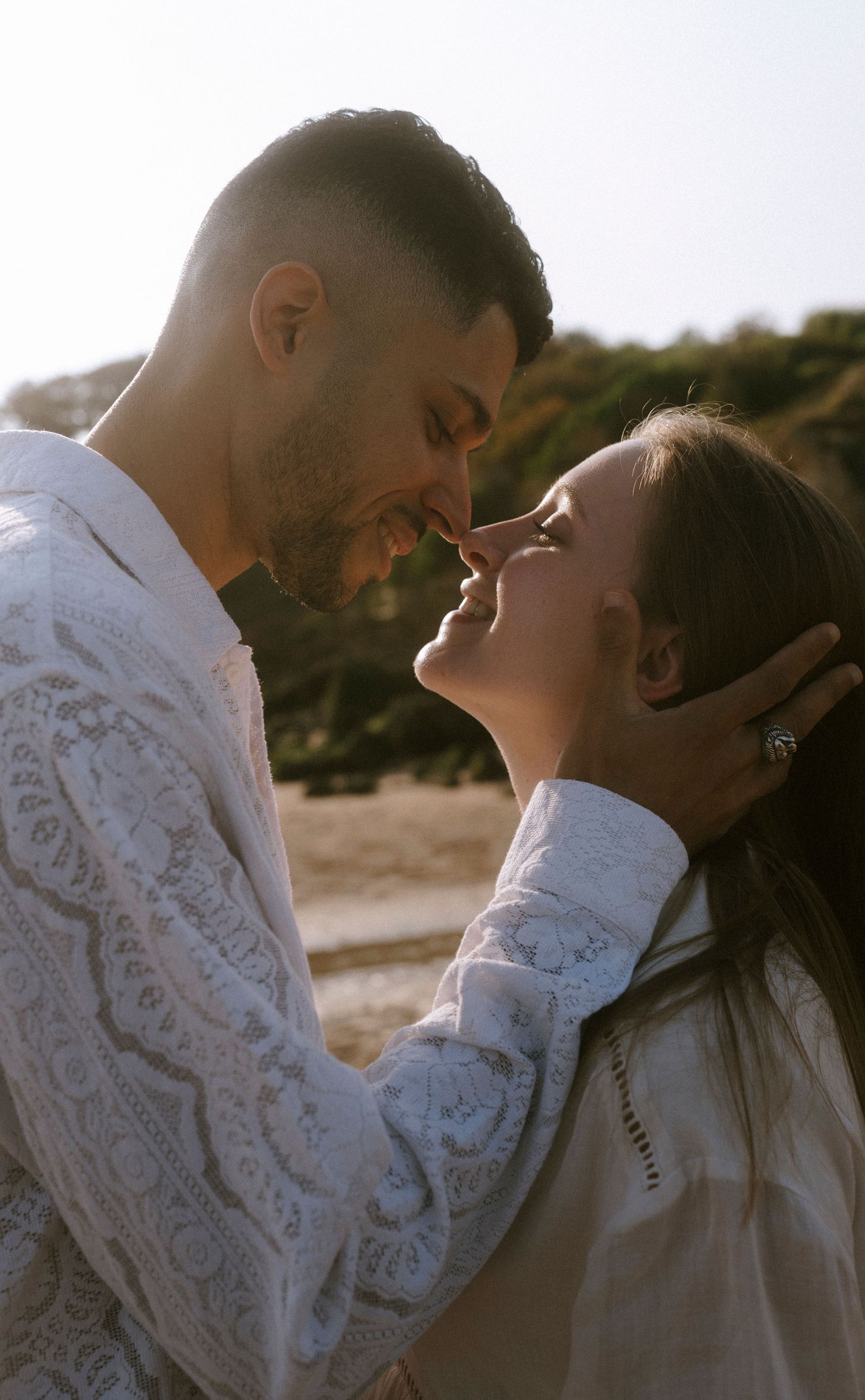 An intimate close-up of a couple in white lace sharing a tender moment on the beach.
